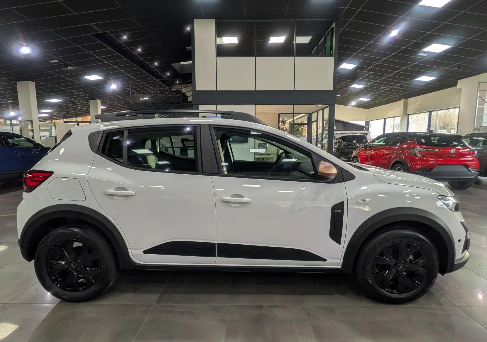 Profil droit d'une Dacia Sandero Stepway TCe 110 blanche Glacier avec jantes noires et protections latérales noires.