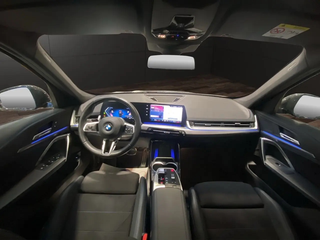 Intérieur avant d'une BMW X1 2025 avec tableau de bord numérique, écran tactile et éclairage d'ambiance bleu.