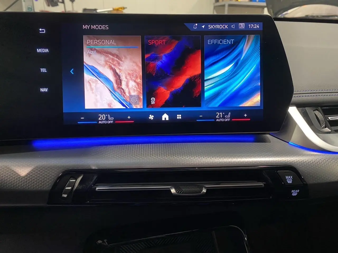 Écran tactile central du tableau de bord du BMW X1 2025 avec ambiance lumineuse bleue et commandes climatisation visibles.