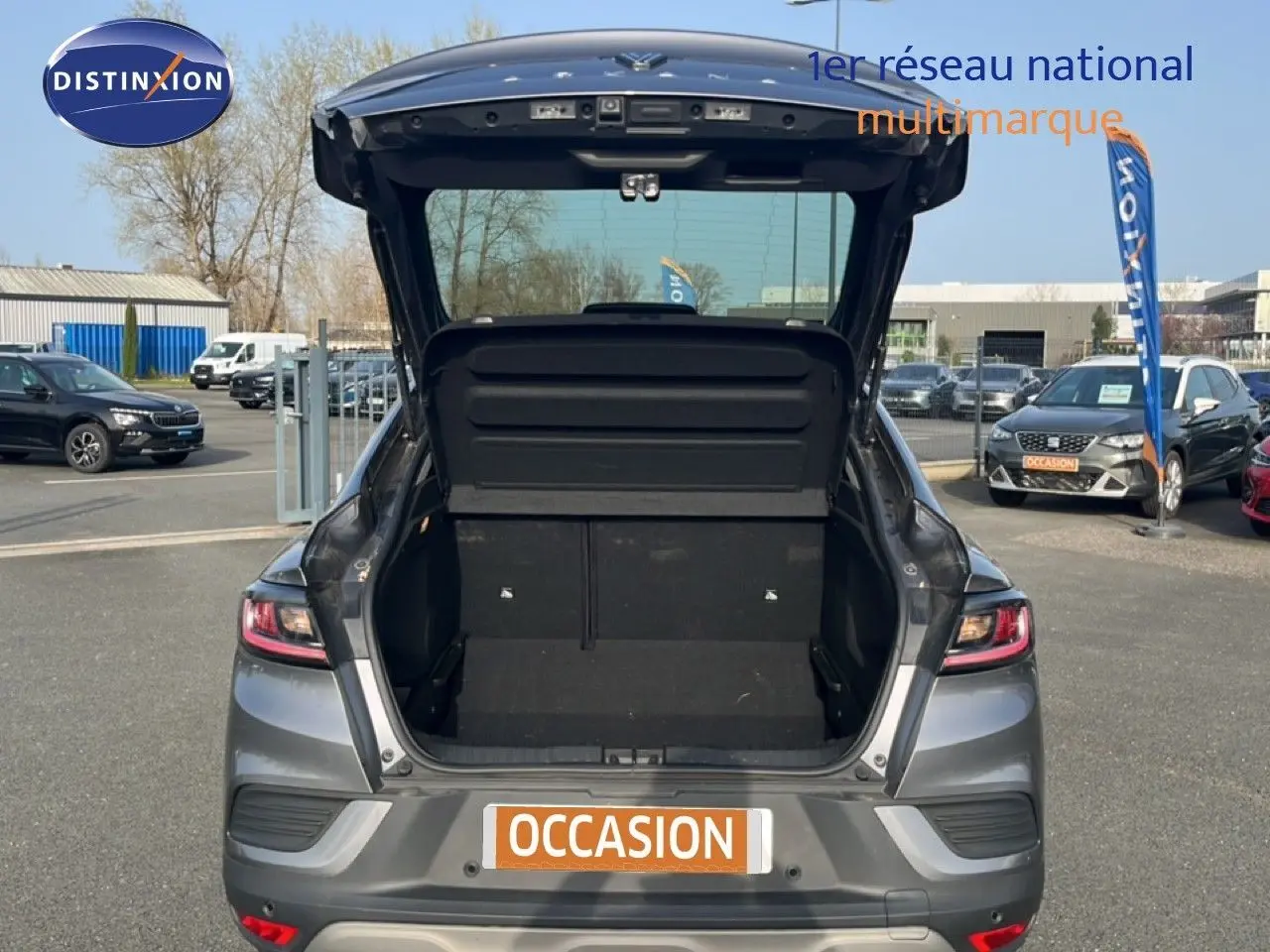 Vue arrière avec coffre ouvert d'une Renault Arkana gris satin métal 2025 sur parking extérieur.