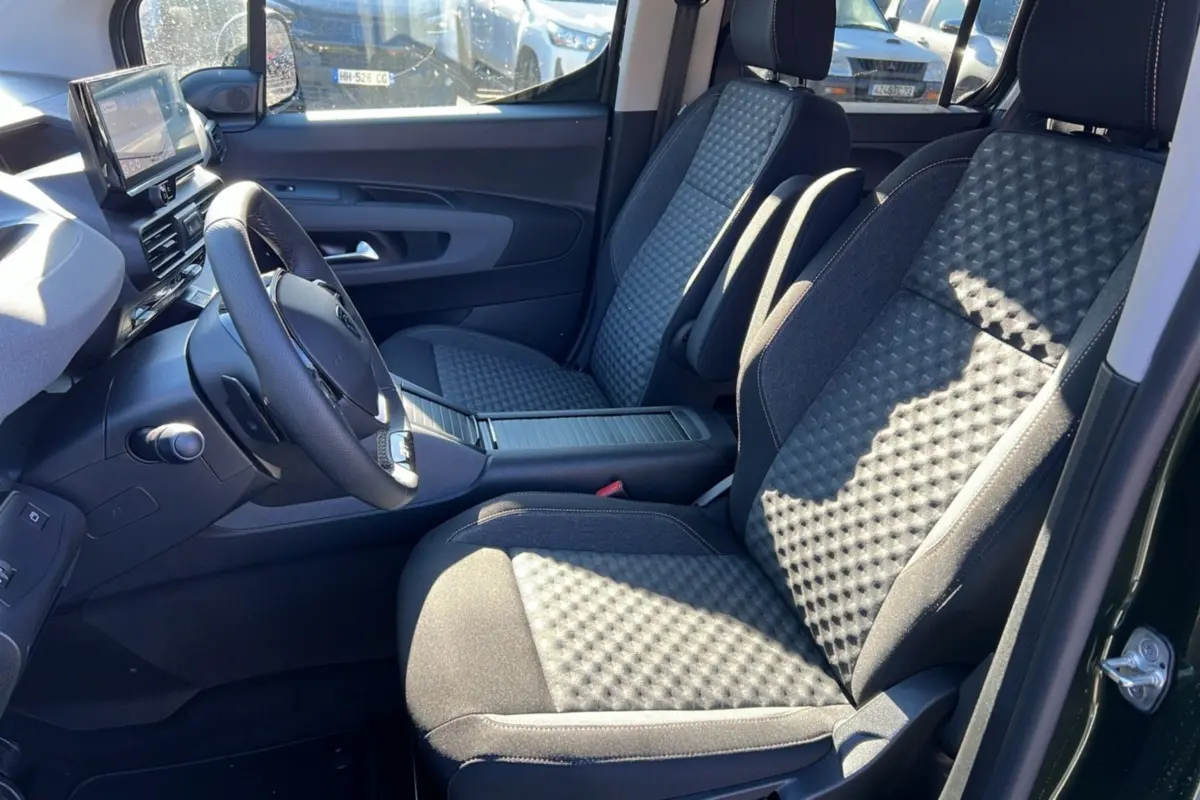 Vue intérieure côté conducteur du Peugeot Rifter 2025 vert sirkka, mettant en valeur les sièges tissu et le volant cuir multifonctions.