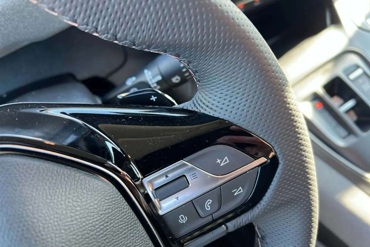 Gros plan sur les commandes multifonctions en plastique noir et gris du volant cuir perforé du Peugeot Rifter 2025.