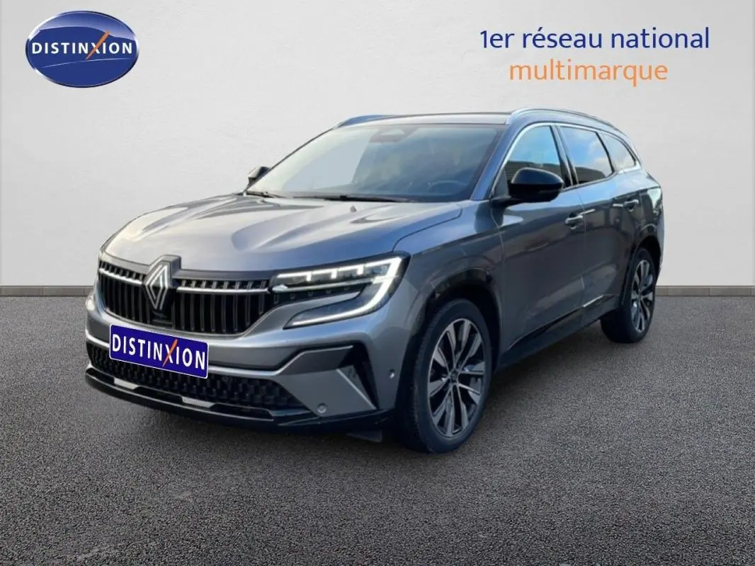 Renault Espace gris 2024 en 3/4 avant droit, avec jantes aluminium et barres de toit visibles.