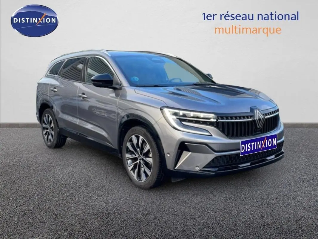 Renault Espace gris 2024 en 3/4 avant droit, avec barres de toit et jantes aluminium distinctives.