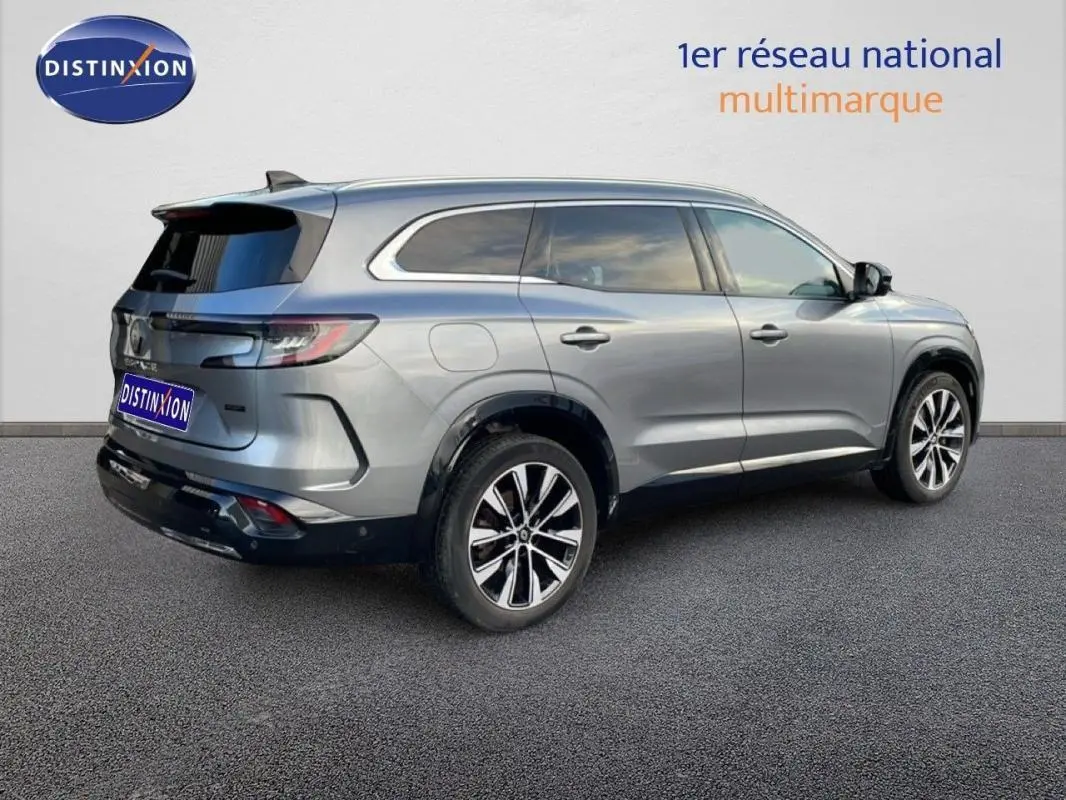 Vue 3/4 arrière droite d'un Renault Espace gris 2024 avec jantes aluminium et barres de toit visibles.