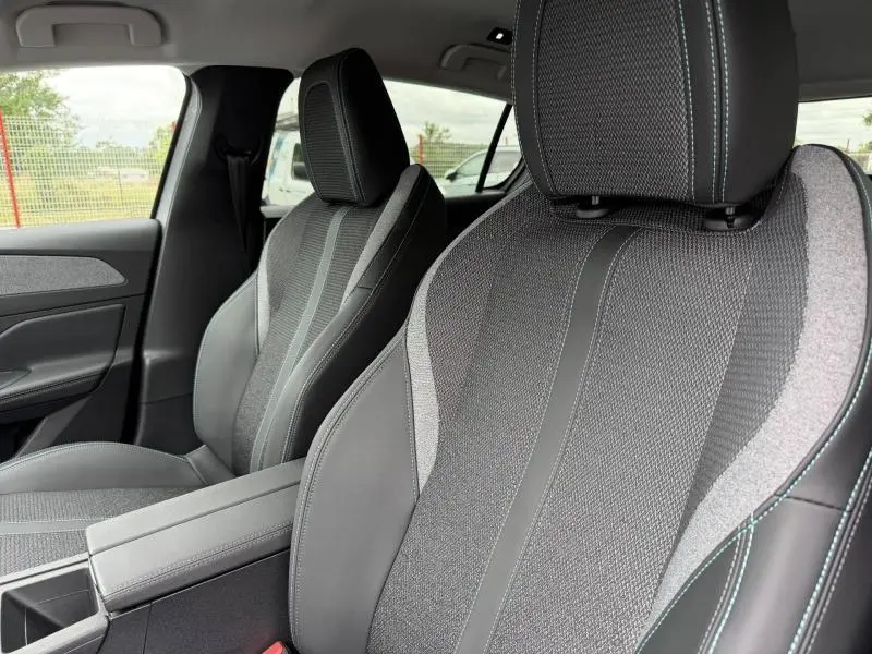Vue intérieure des sièges avant en tissu et cuir noir avec surpiqûres bleues de la Peugeot 308 Hybrid 2025.