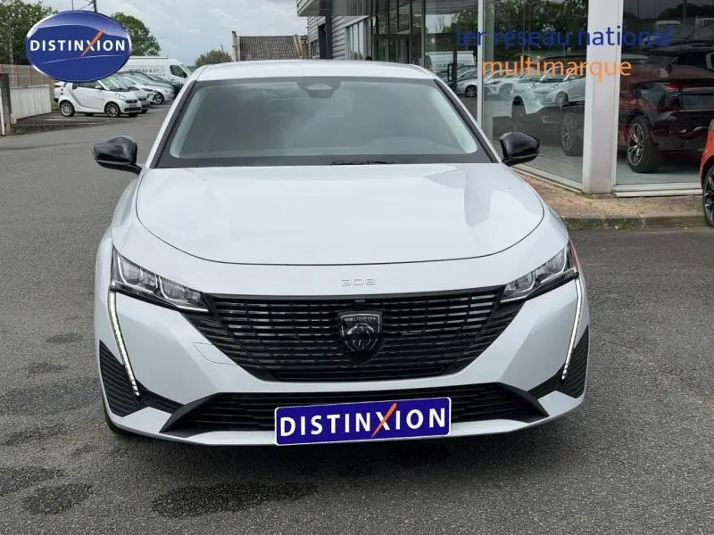 Vue frontale d'une Peugeot 308 blanche Okénite avec calandre noire et feux LED verticaux distinctifs.