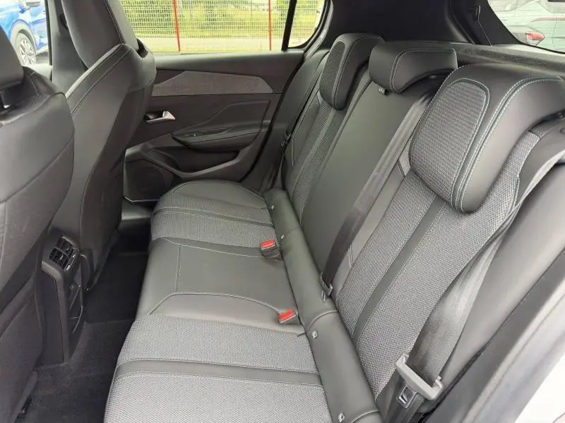 Vue latérale intérieure arrière droite de la Peugeot 308 1.2 Hybrid 145ch Allure avec banquette tissu noir et ceintures de sécurité.