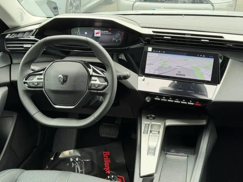Vue intérieure centrée sur le volant et le tableau de bord numérique de la Peugeot 308 hybride 2025, avec écran tactile GPS.