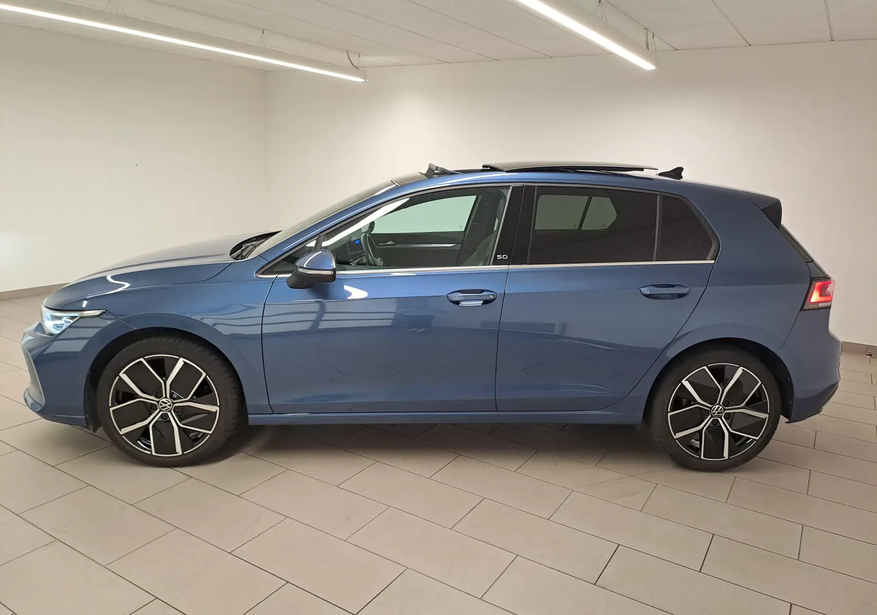 Profil droit d'une Volkswagen Golf 1.5 eTSI 150 DSG7 Edition 50 en bleu Anémone avec toit ouvrant panoramique et jantes stylées.