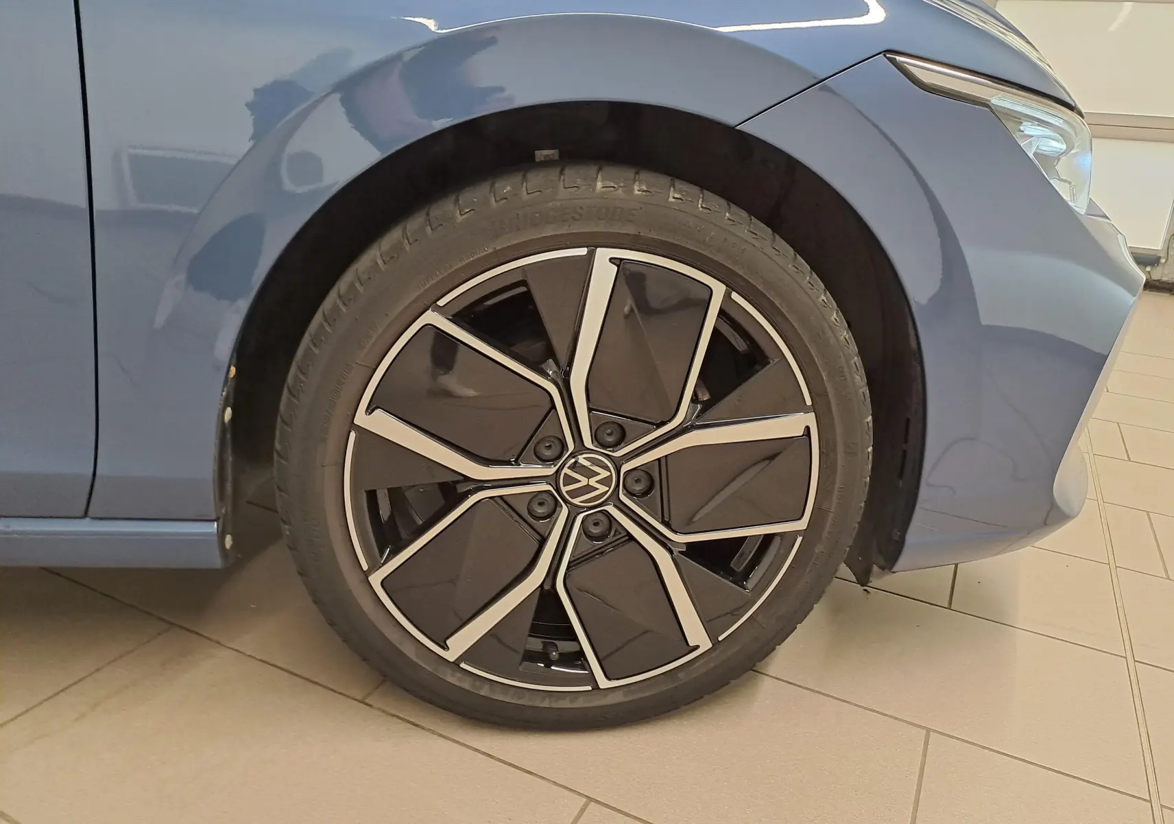 Gros plan sur la roue avant gauche de la Volkswagen Golf 1.5 eTSI 150 DSG7 Bleu Anémone avec jante noire et argentée.