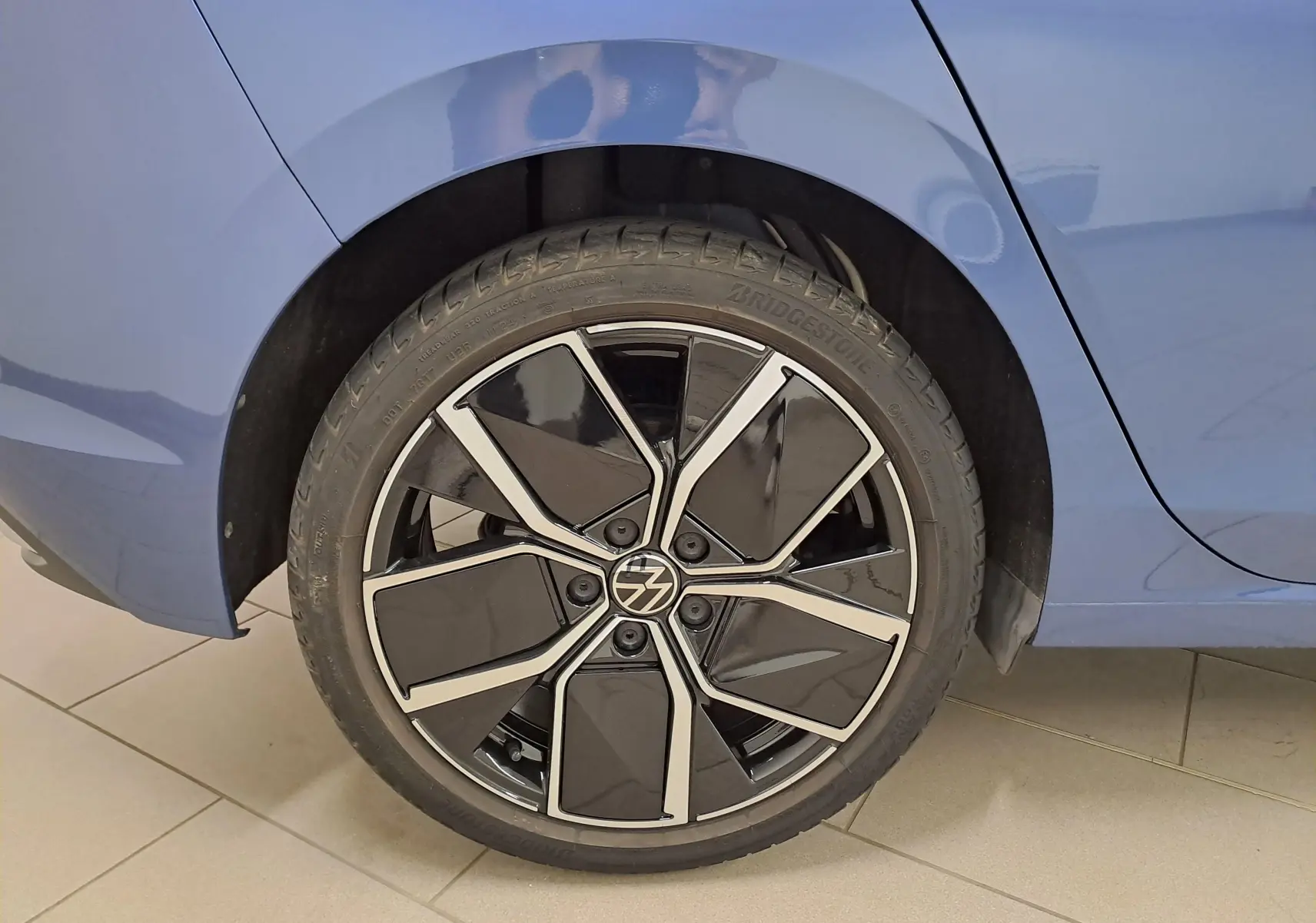 Gros plan sur la roue arrière droite d'une Volkswagen Golf 1.5 eTSI Bleu Anémone avec jante noire et argentée.