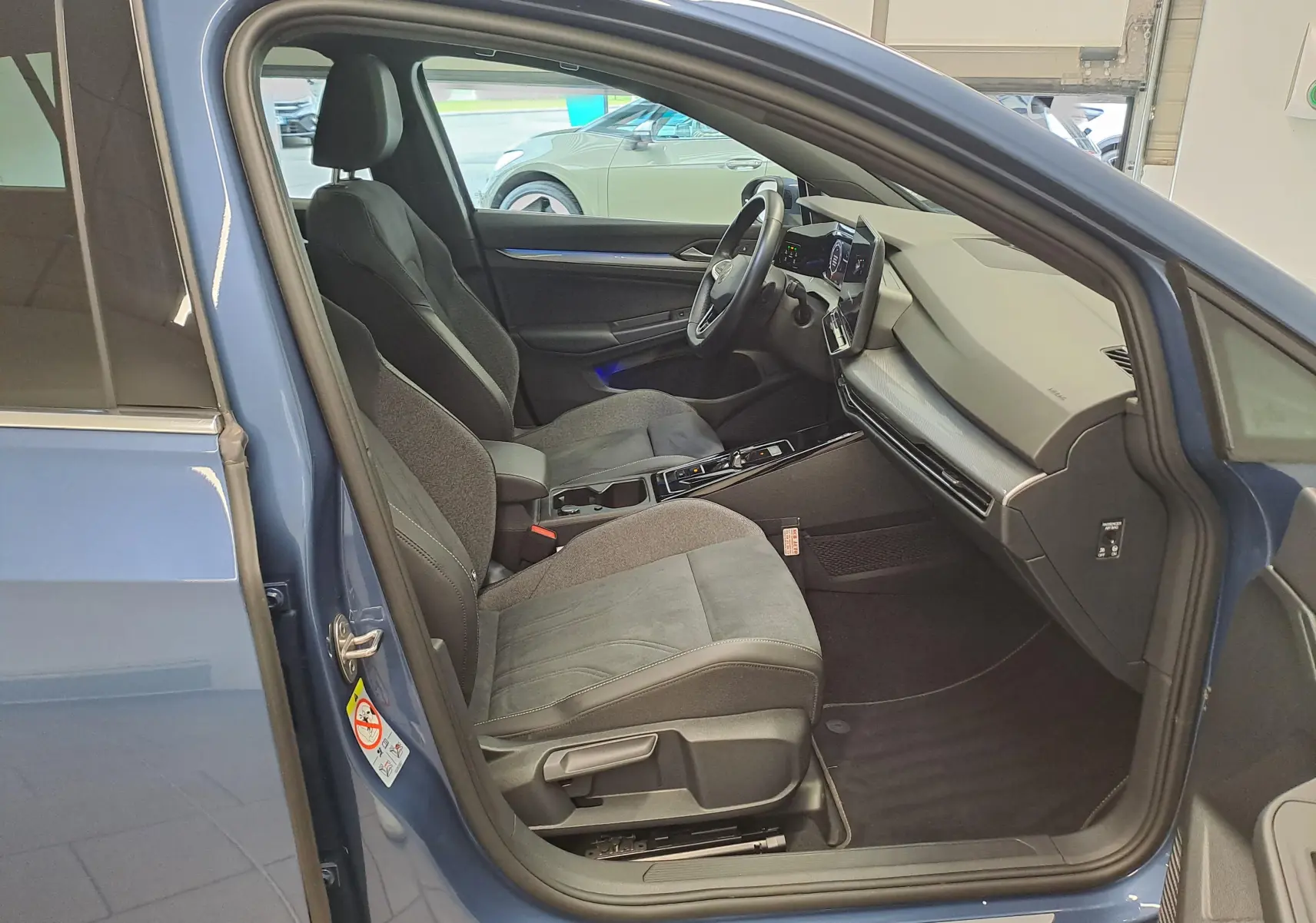 Vue intérieure côté conducteur de la Volkswagen Golf 1.5 eTSI 150 Bleu Anémone, mettant en valeur les sièges et le tableau de bord moderne.