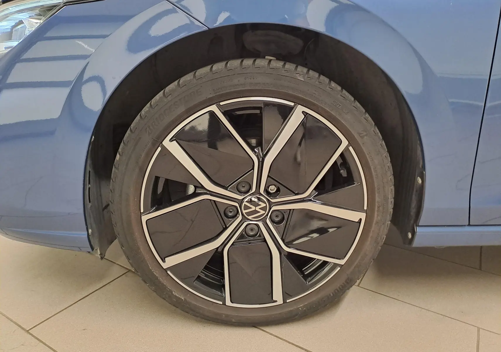 Gros plan sur la roue avant gauche de la Volkswagen Golf Bleu Anémone avec jante alliage noire et argentée.