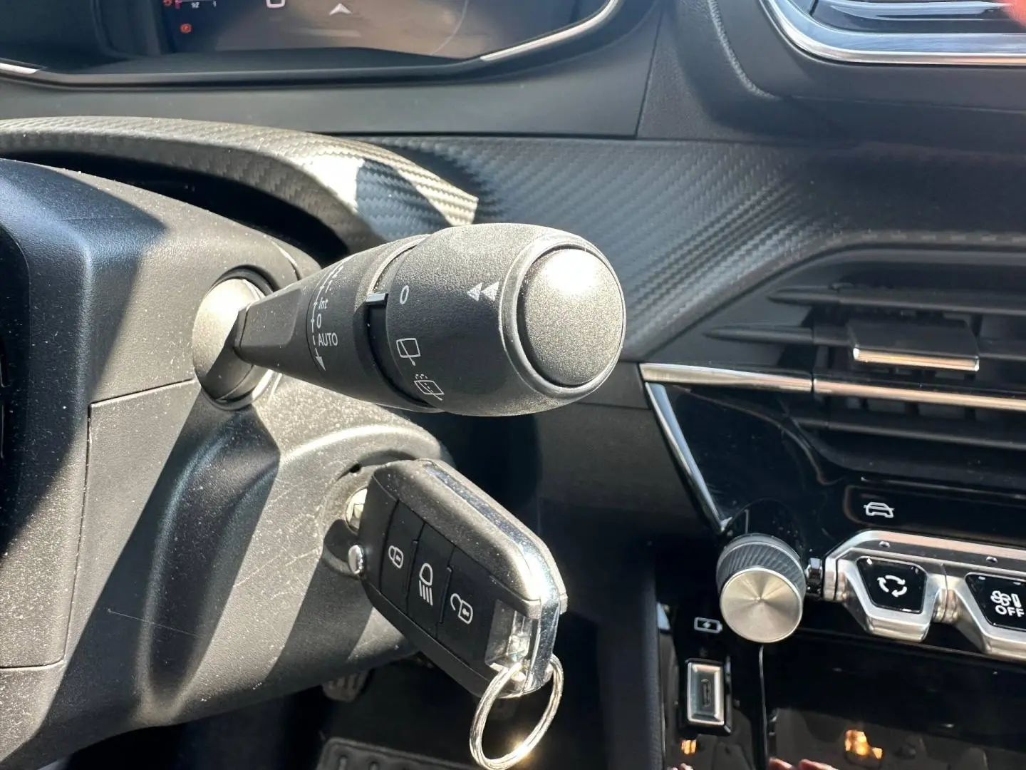 Gros plan sur le contacteur avec clé insérée dans une Peugeot 208 gris Selenium, tableau de bord noir et commandes centrales visibles.