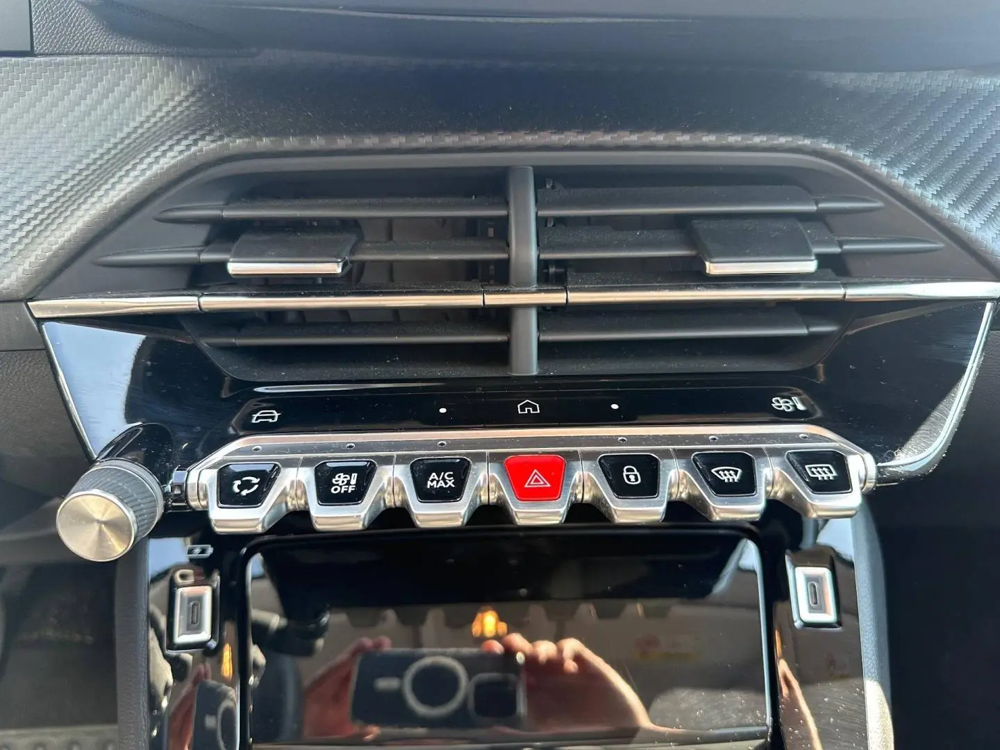Gros plan sur la console centrale de la Peugeot 208 2025, boutons chromés et écran tactile noir brillant.