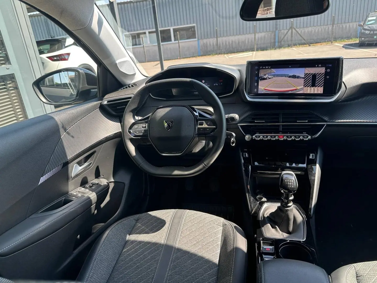 Vue intérieure avant de la Peugeot 208 1.2 100ch gris Selenium, volant compact et écran tactile avec caméra de recul.