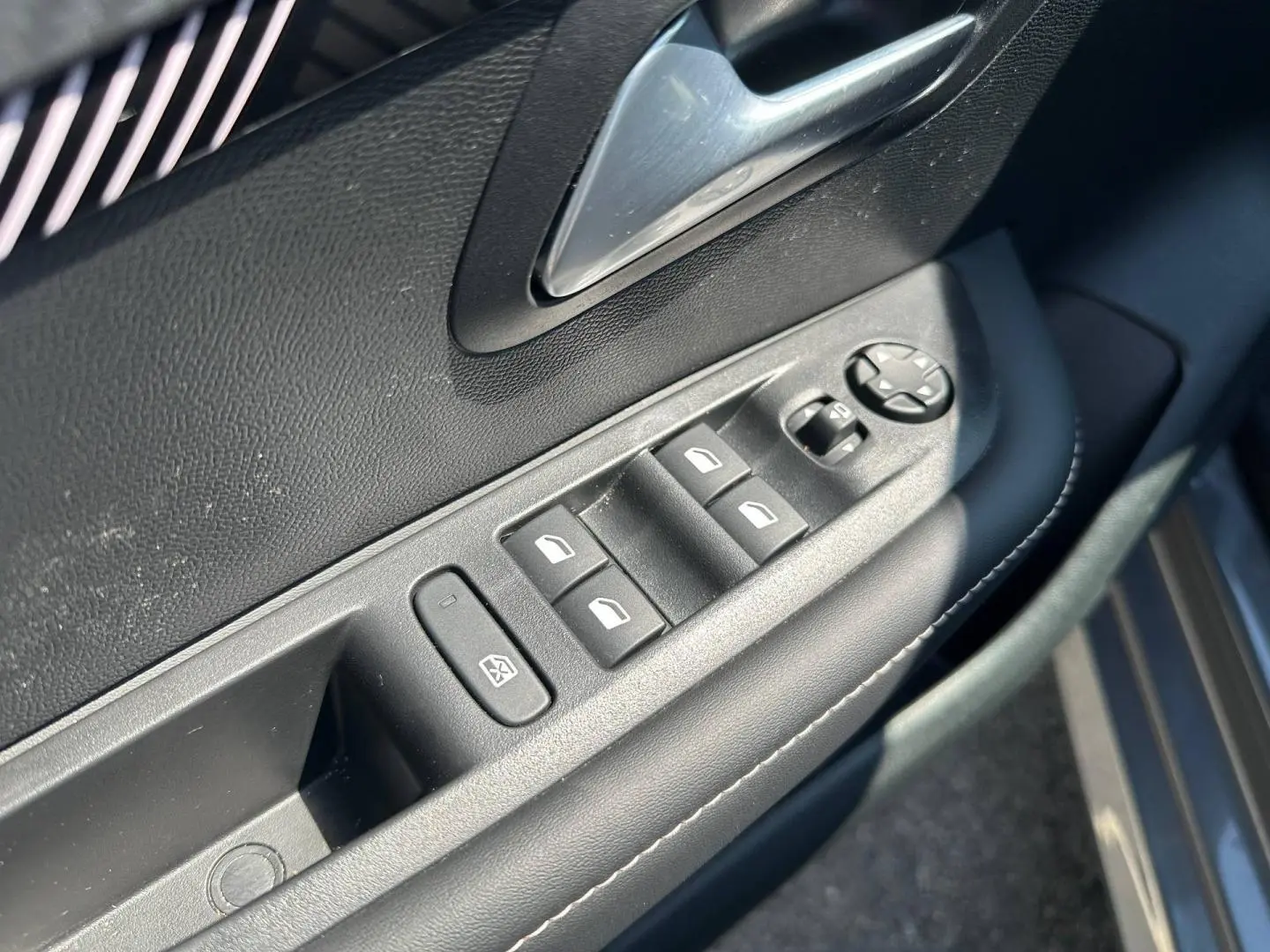 Détail des commandes de lève-vitres et rétroviseurs sur la porte côté gauche d’une Peugeot 208 gris Selenium.
