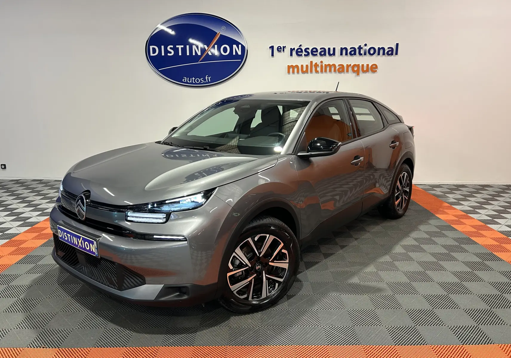 Citroën E-C4 électrique gris foncé en 3/4 avant droit, avec jantes noires et phares LED allumés en showroom.