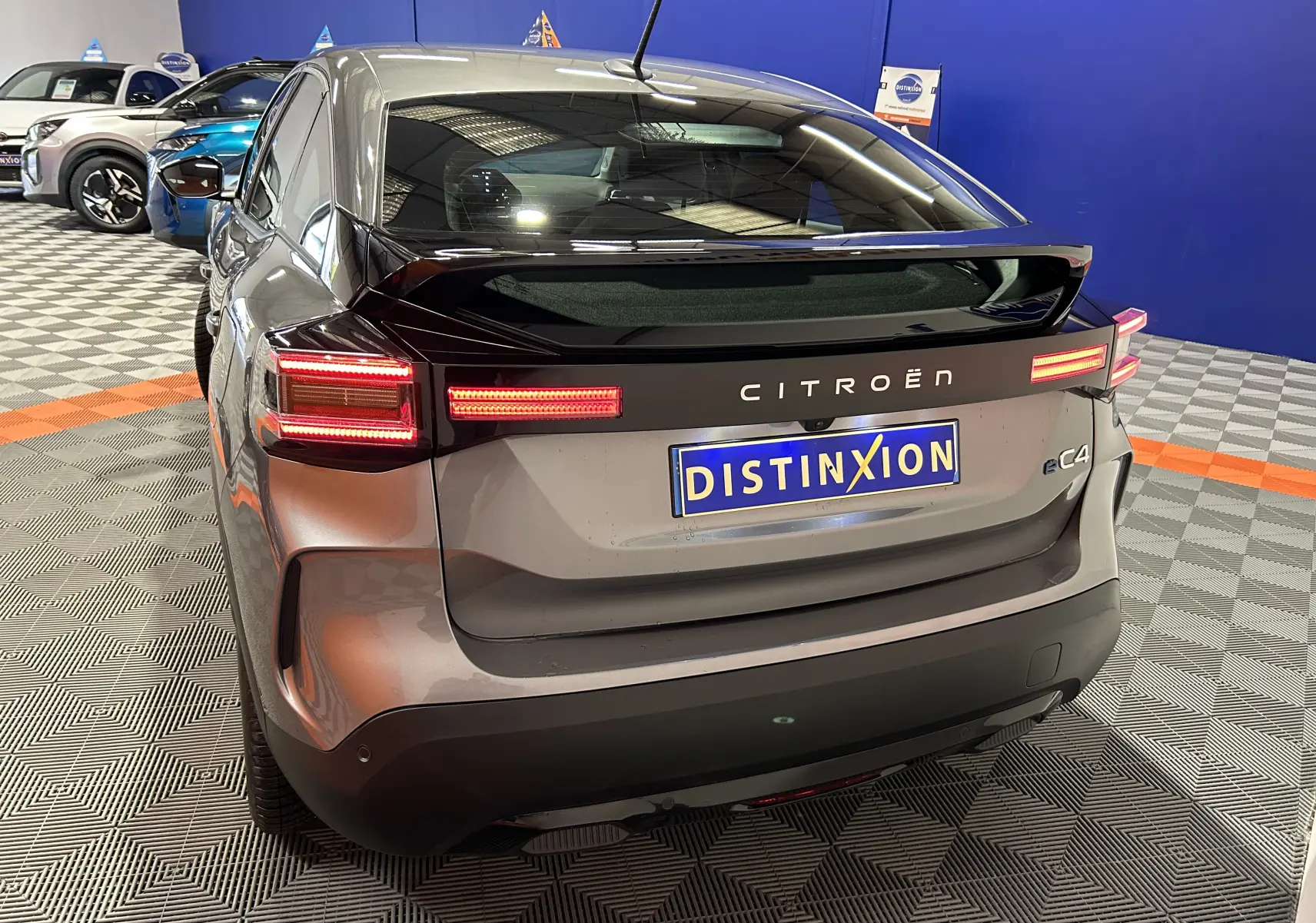 Vue 3/4 arrière droite d'une Citroën E-C4 électrique gris foncé avec feux LED allumés dans un showroom.