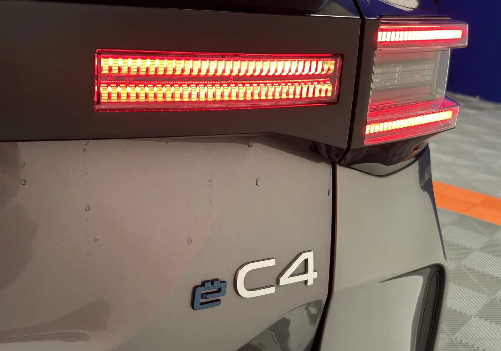 Gros plan sur le feu arrière droit rouge allumé et l’inscription e-C4 sur la carrosserie gris foncé d’une Citroën électrique.