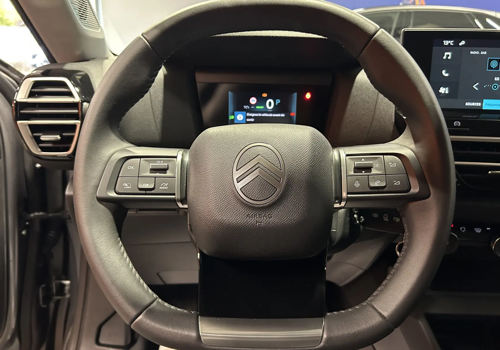 Vue frontale du volant noir du Citroën E-C4 électrique 2025 avec commandes intégrées et tableau de bord numérique en arrière-plan.