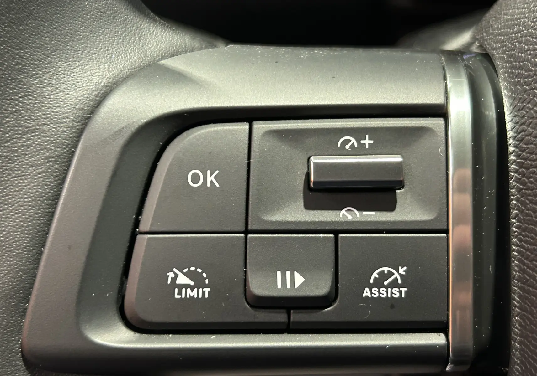 Gros plan sur les commandes de régulateur de vitesse du Citroën E-C4 gris foncé, boutons noirs avec inscriptions blanches.
