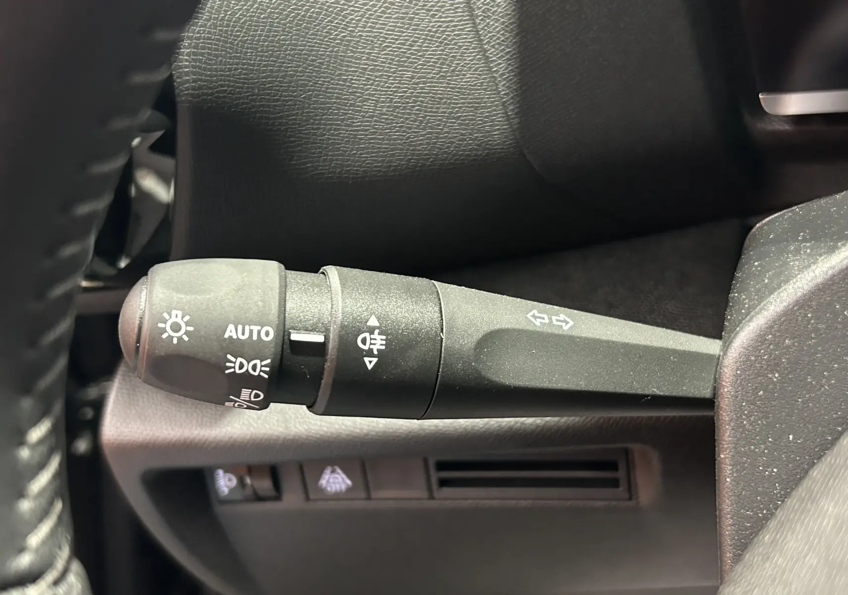 Gros plan sur la commande de clignotants et phares à gauche du volant dans l’habitacle d’une Citroën E-C4 gris foncé.
