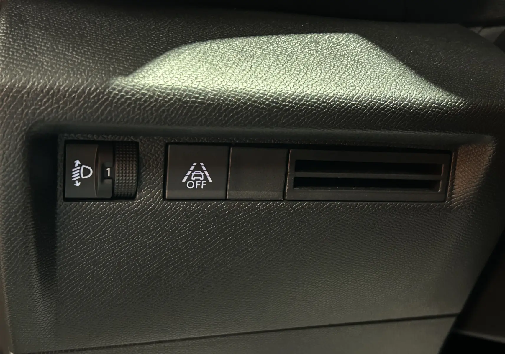 Détail intérieur du tableau de bord côté gauche du Citroën E-C4 2025, avec réglage des phares et bouton de désactivation de l'alerte de franchissement de ligne.