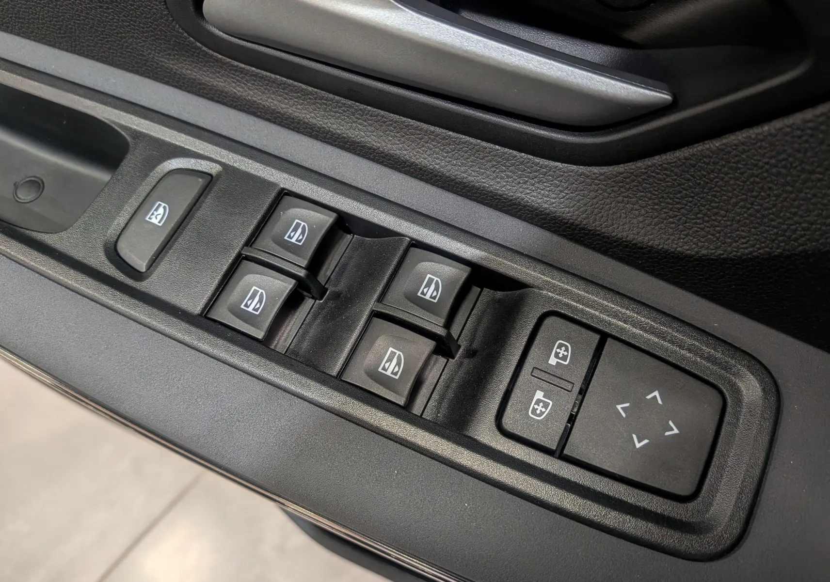 Panneau de commandes des vitres et réglages des rétroviseurs côté conducteur dans une Dacia Sandero Stepway 2025 gris schiste.