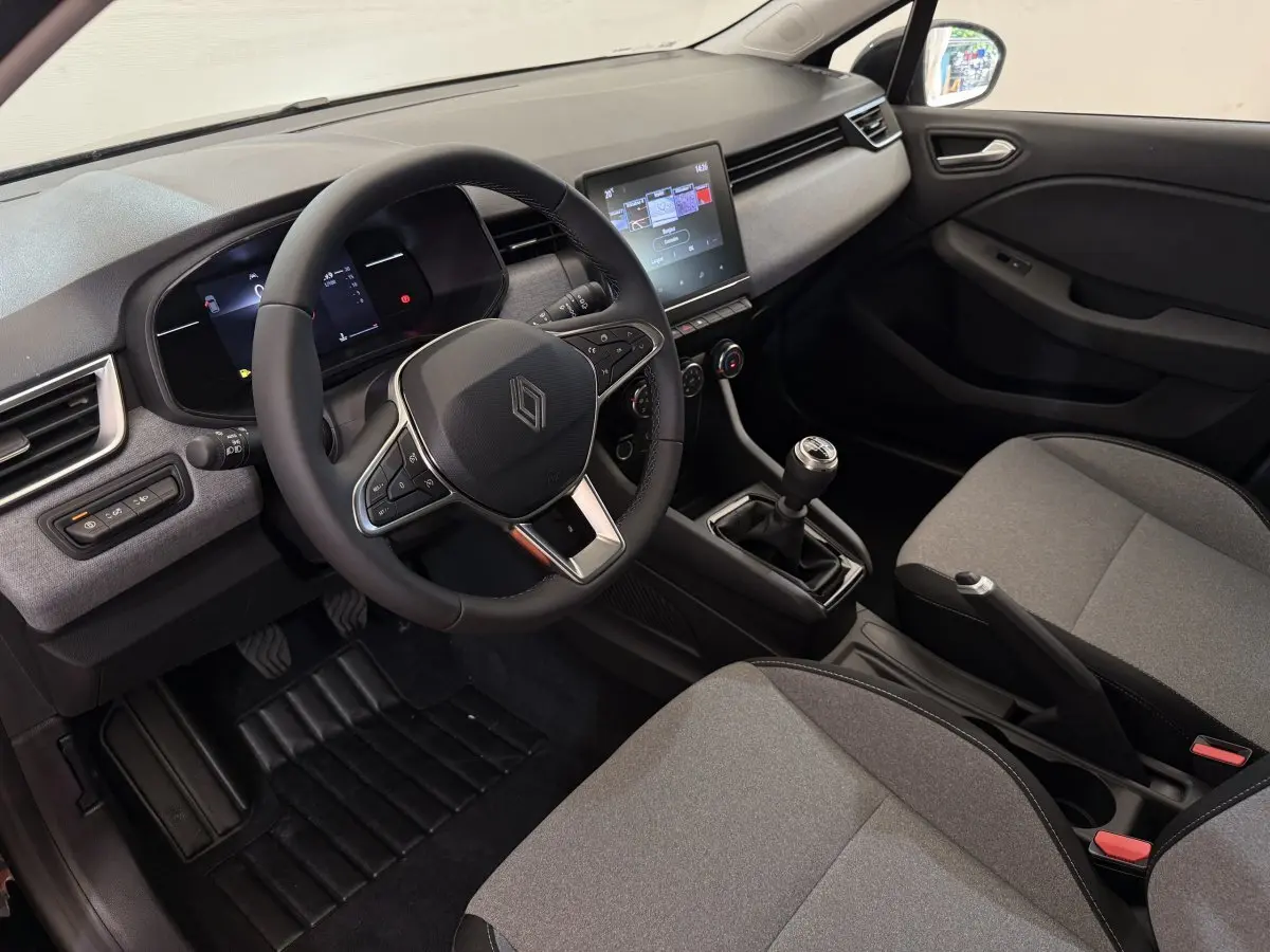Intérieur Renault Clio 2025 vu côté conducteur, volant cuir, écran tactile central et sièges gris clair.