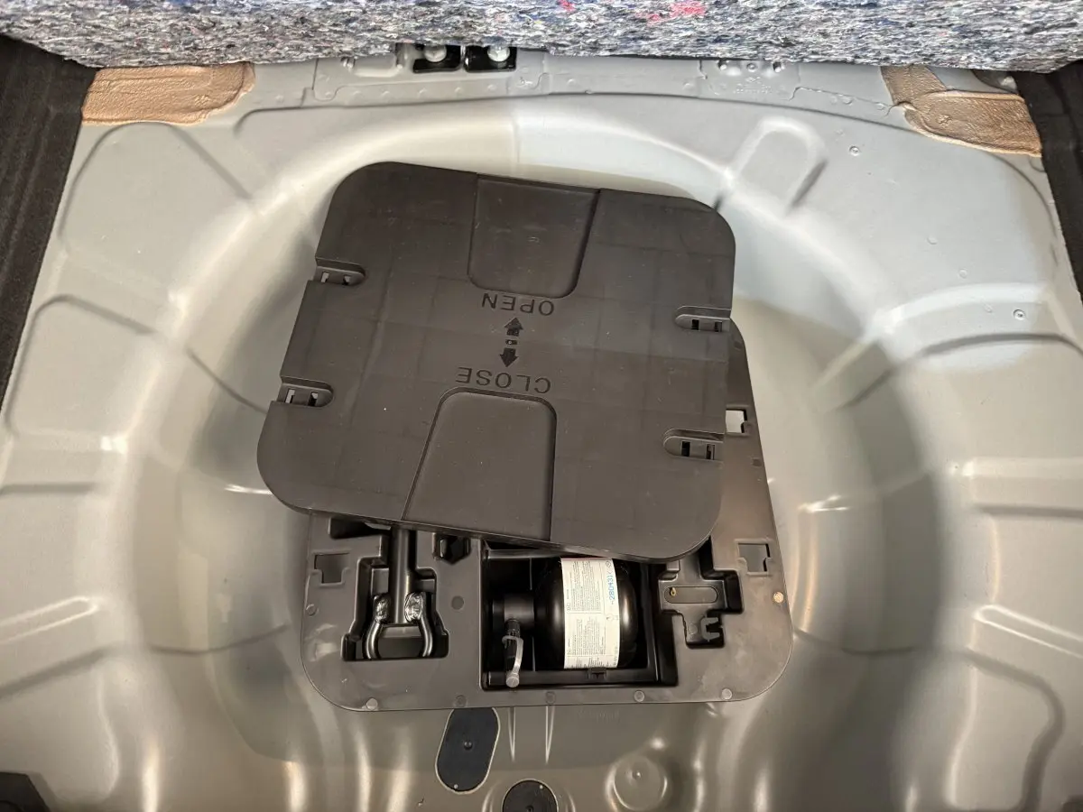 Vue plongeante sur le compartiment de rangement sous le plancher du coffre de la Renault Clio noire 2025.