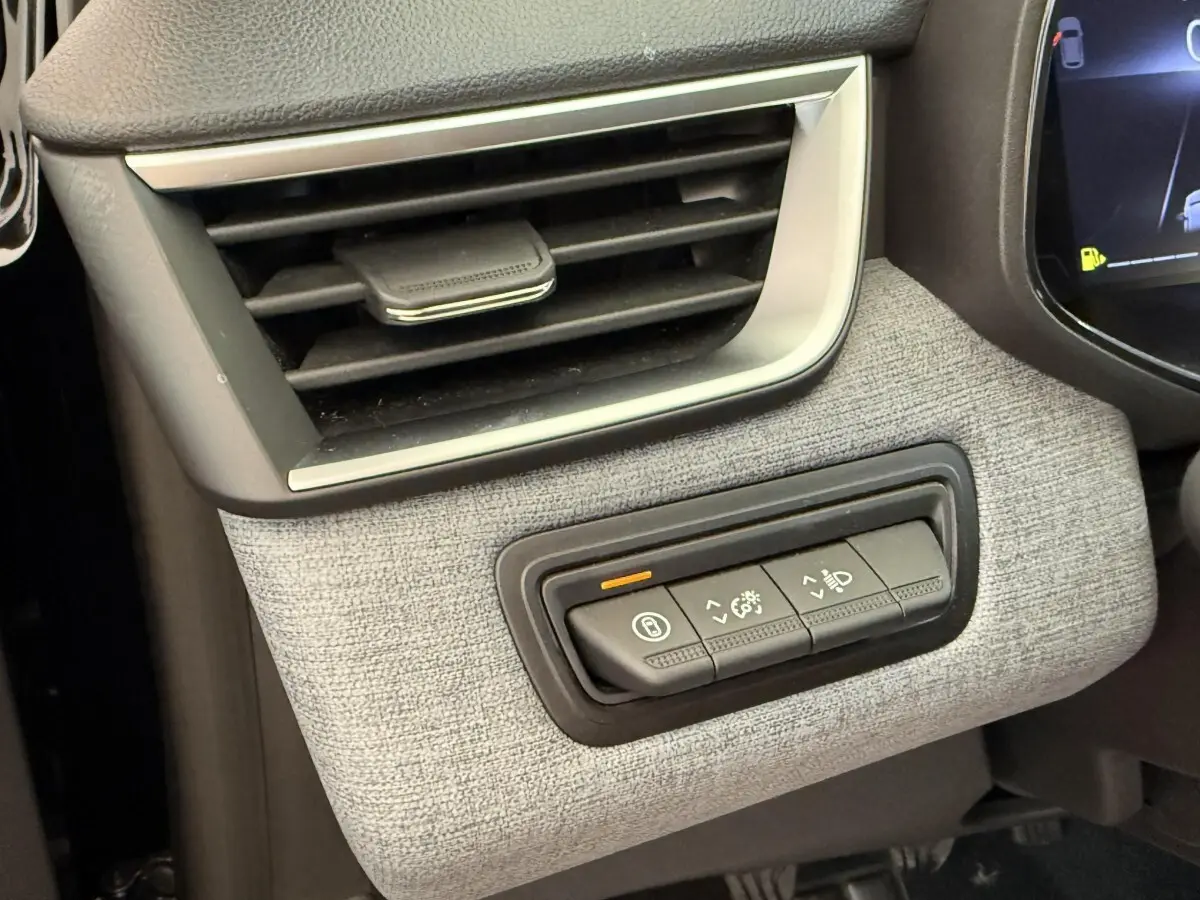 Gros plan sur la commande d'éclairage et la sortie d'air côté gauche du tableau de bord gris clair d'une Renault Clio noire 2025.