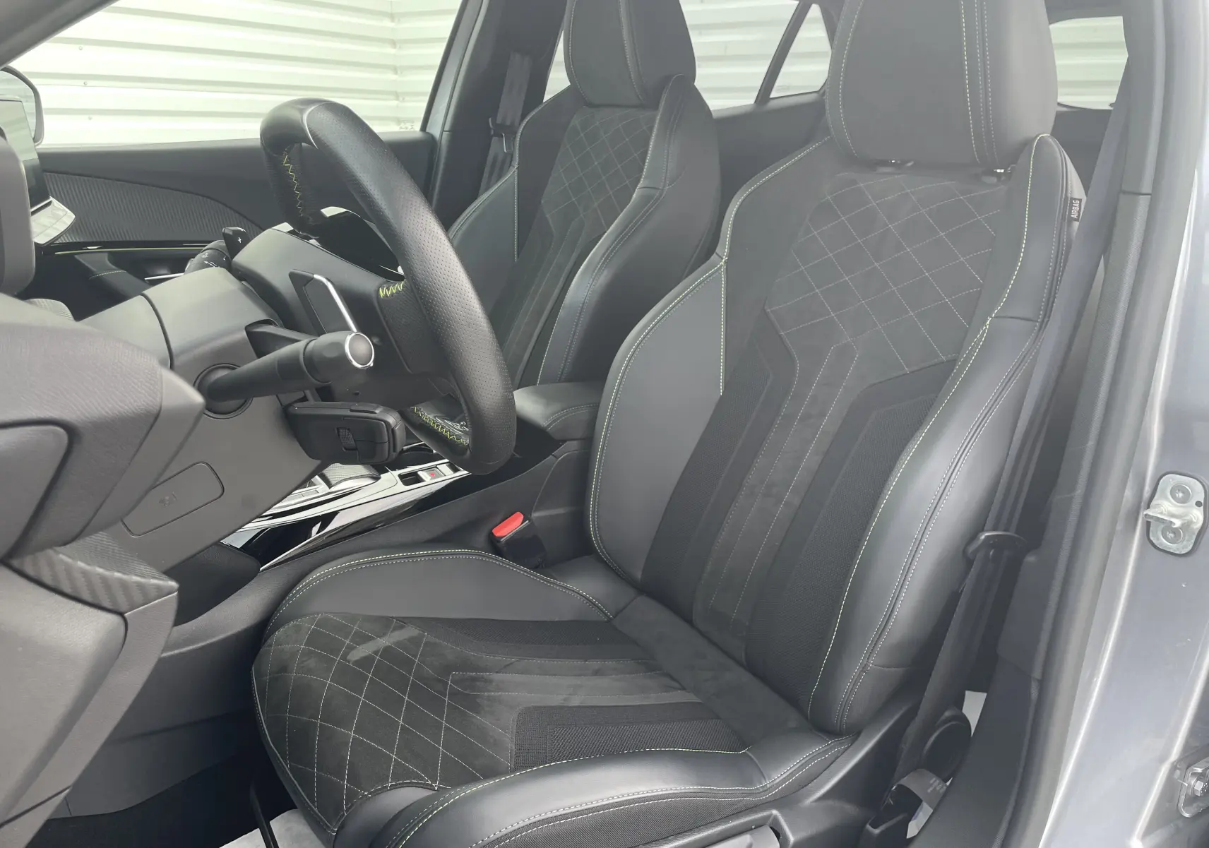 Vue intérieure côté conducteur du Peugeot 2008 gris Artense 2022, sièges sport en cuir et alcantara avec surpiqûres vertes.