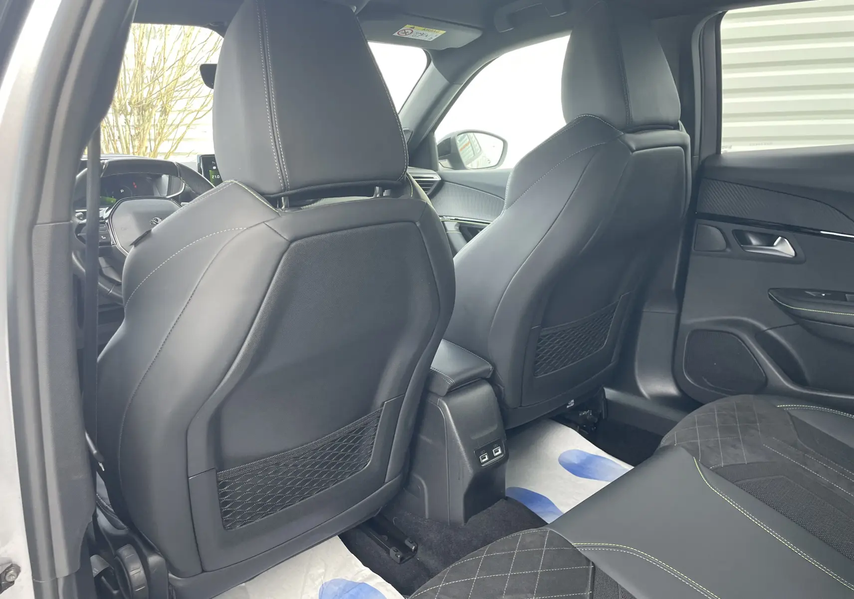 Vue intérieure arrière du Peugeot 2008 gris Artense 2022, sièges avant en cuir noir avec surpiqûres vertes et ports USB centraux.