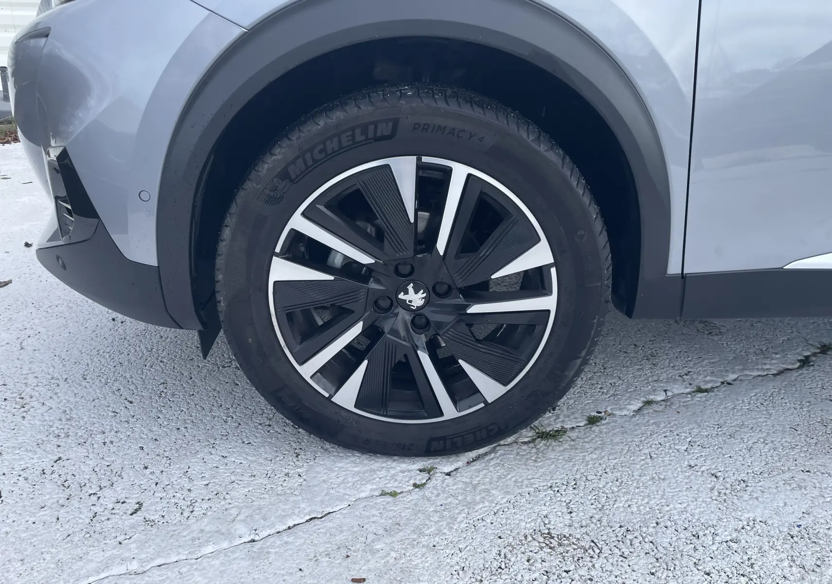 Gros plan sur la roue avant gauche du Peugeot 2008 gris Artense, mettant en valeur la jante alliage bicolore et le pneu Michelin.