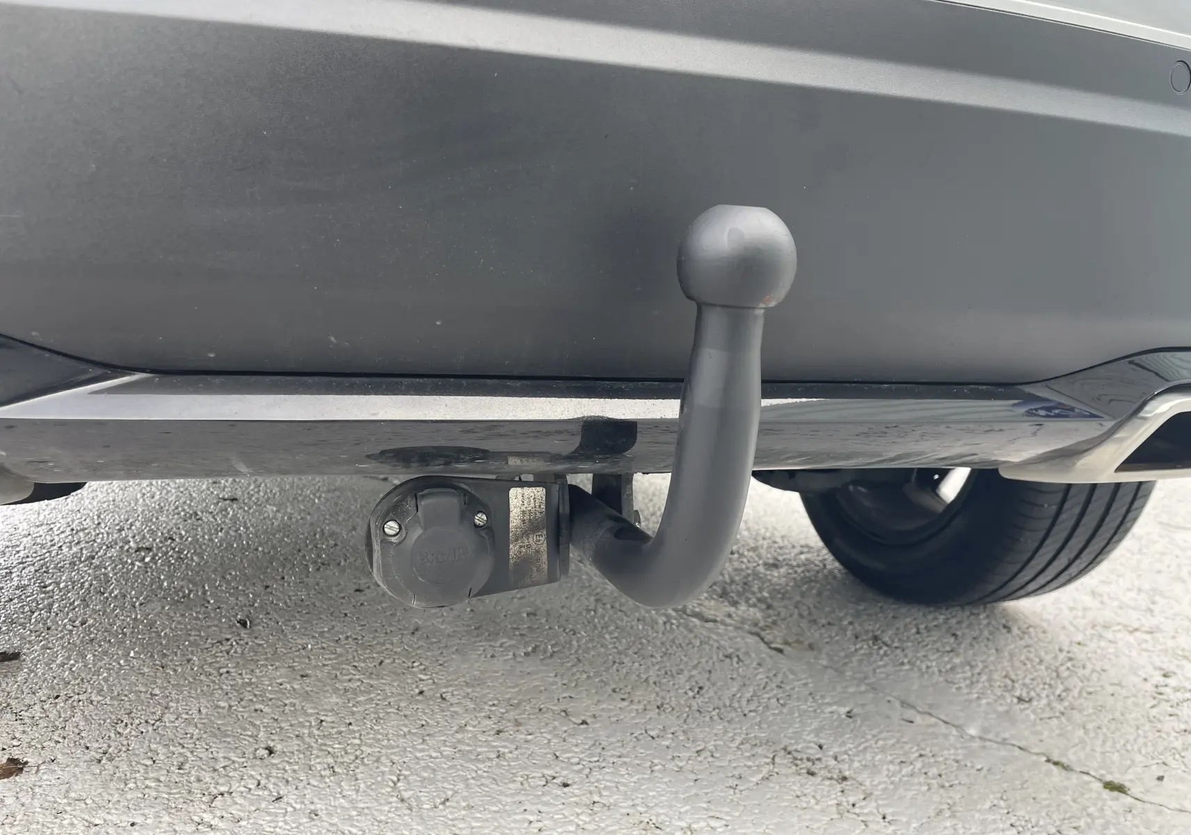 Gros plan sur l'attelage d'une Peugeot 2008 gris Artense, vue arrière basse avec prise électrique visible sous le pare-chocs.