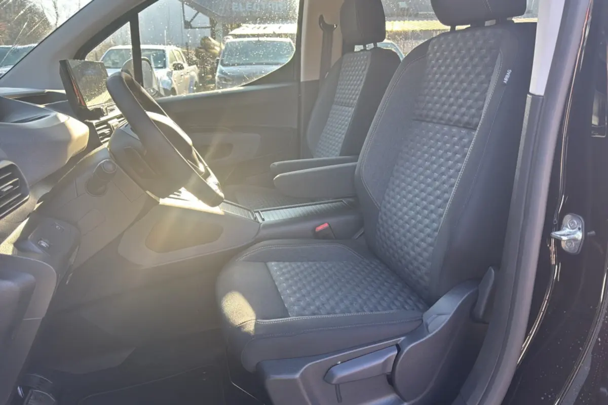 Intérieur avant droit du Peugeot Rifter noir perla nera 2025, sièges tissu gris avec accoudoir central et volant multifonctions.