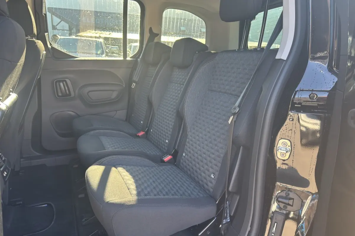 Vue latérale intérieure sur les sièges arrière tissu gris du Peugeot Rifter Noir Perla Nera 2025 avec porte ouverte.