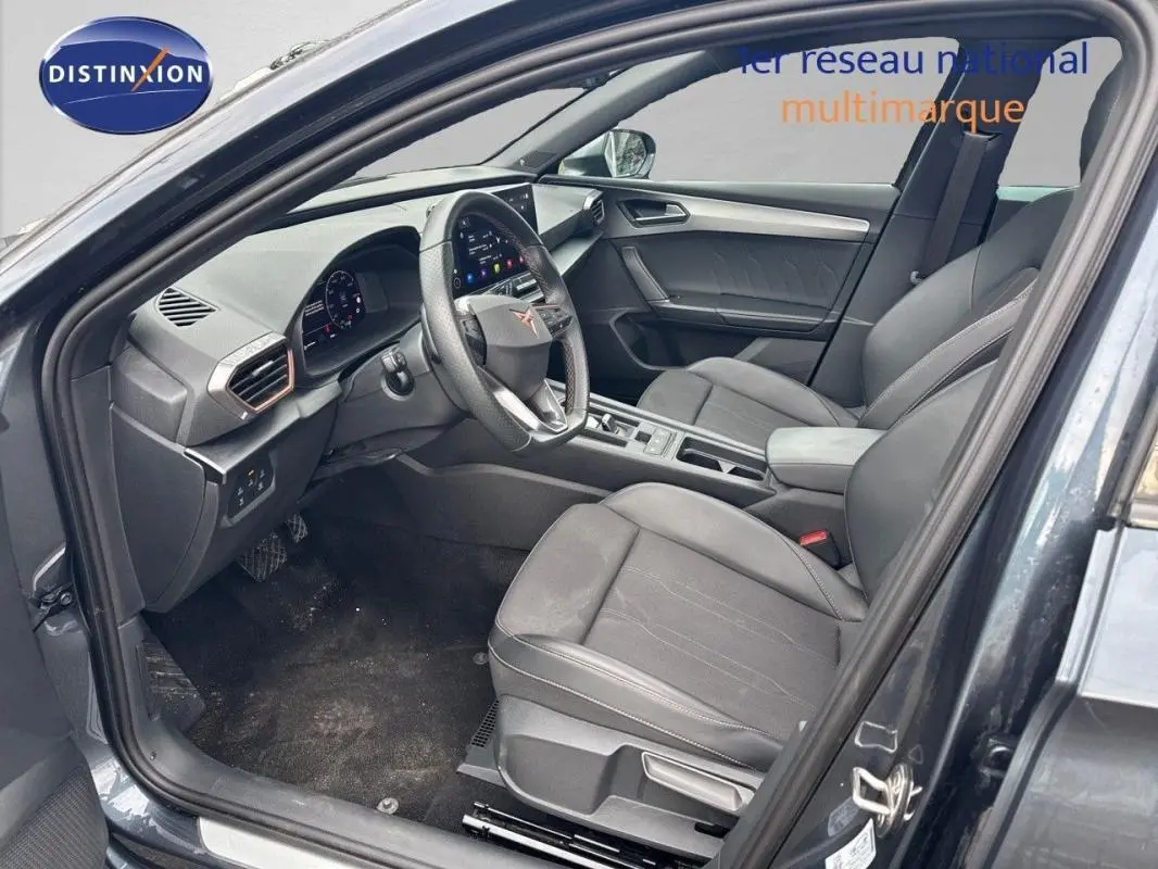 Vue intérieure côté conducteur d'une CUPRA Leon ST gris 2024 avec tableau de bord numérique et volant cuir.