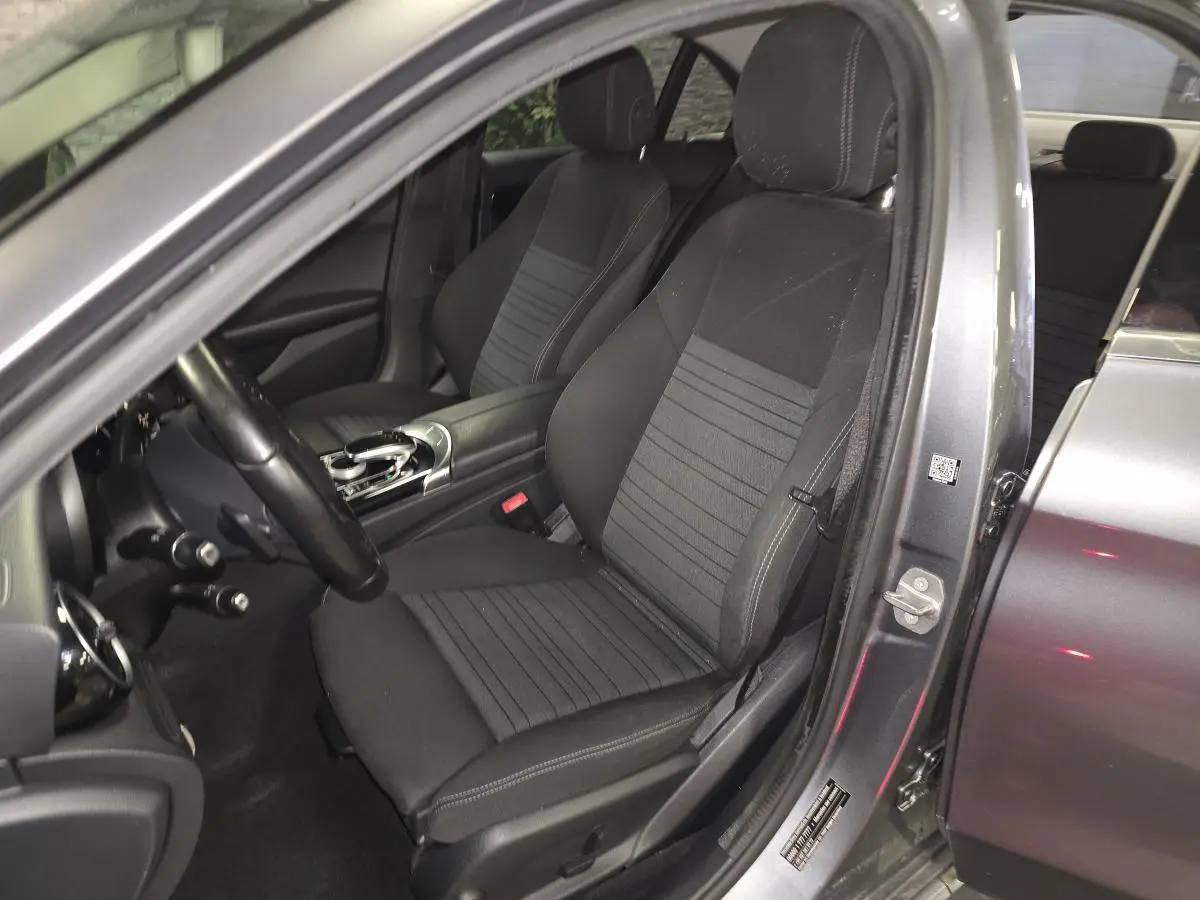 Vue intérieure côté conducteur d'une Mercedes Classe C gris métallisé, sièges avant en tissu noir avec console centrale.