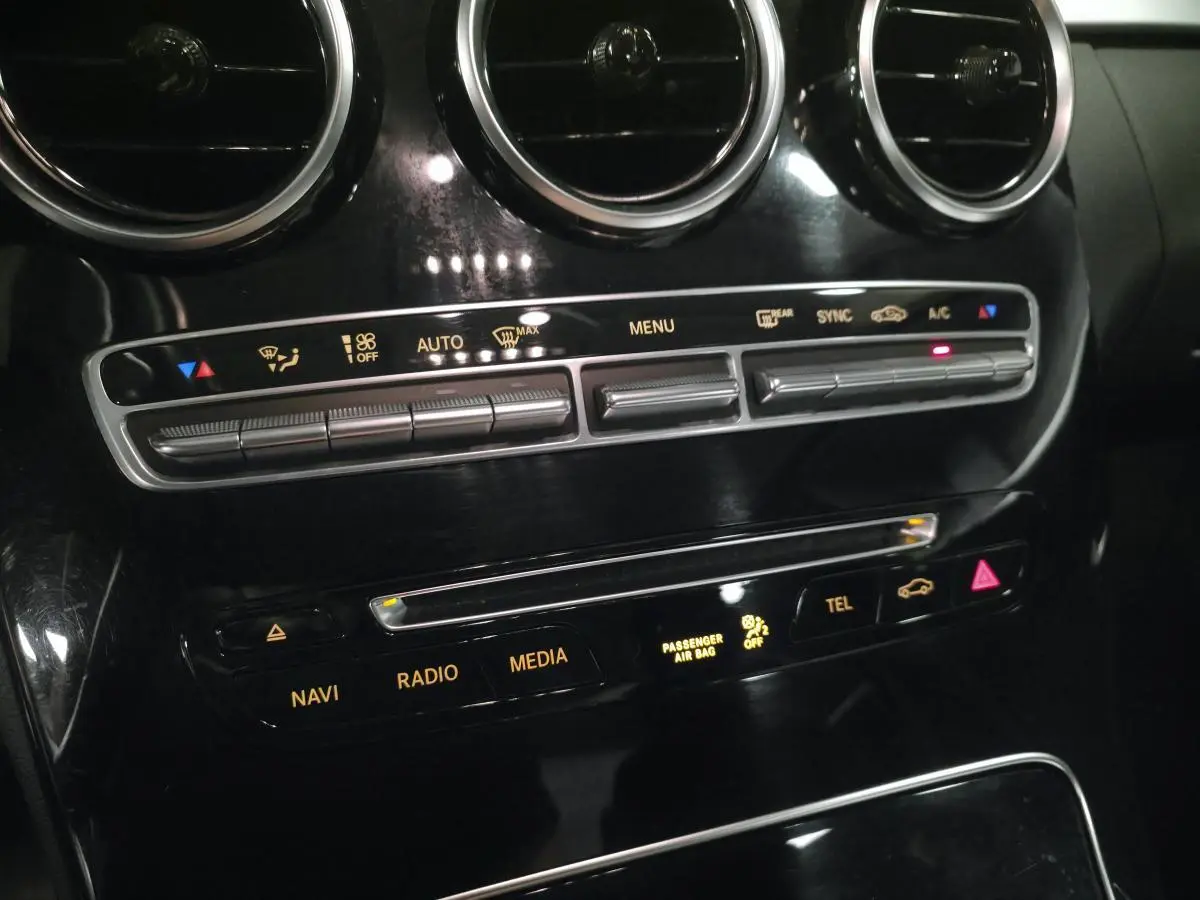 Gros plan sur la console centrale noire brillante de la Mercedes Classe C 200 d, avec commandes climatisation et multimédia.