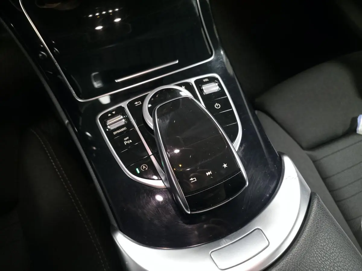 Vue rapprochée de la console centrale noire brillante avec pavé tactile et commandes sur Mercedes Classe C gris.