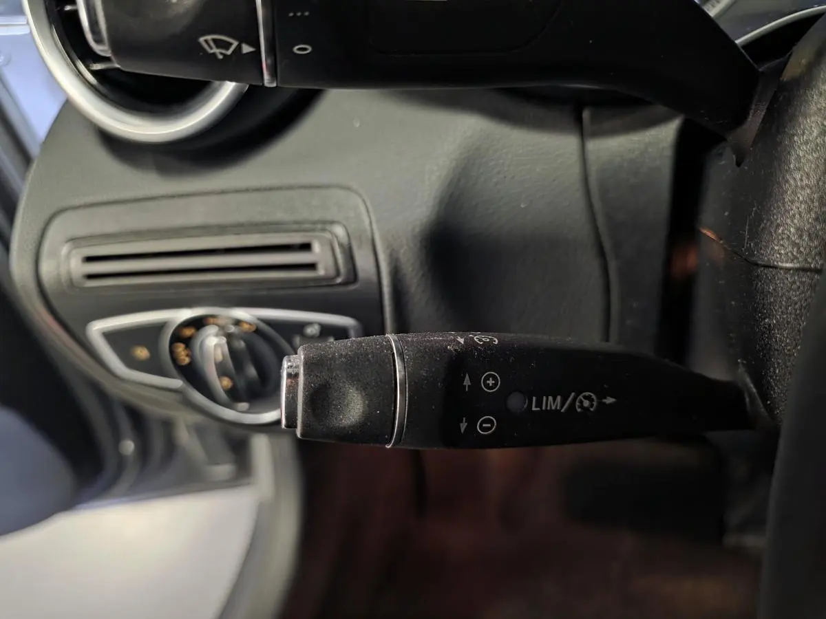 Gros plan sur la commande de régulateur de vitesse à gauche du volant dans l’habitacle noir d’une Mercedes Classe C gris métallisé.