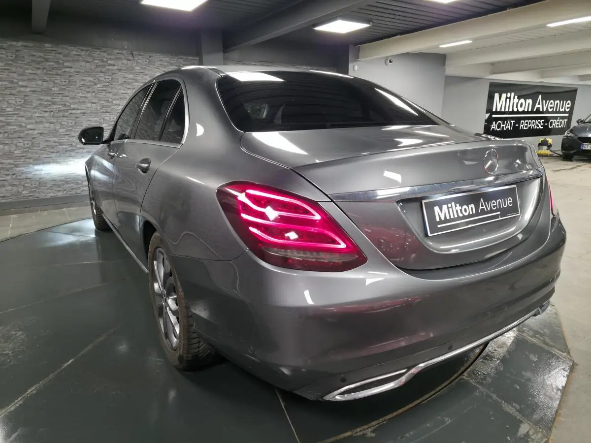 Vue 3/4 arrière gauche d'une Mercedes Classe C gris métallisé avec feux arrière LED allumés en intérieur showroom.
