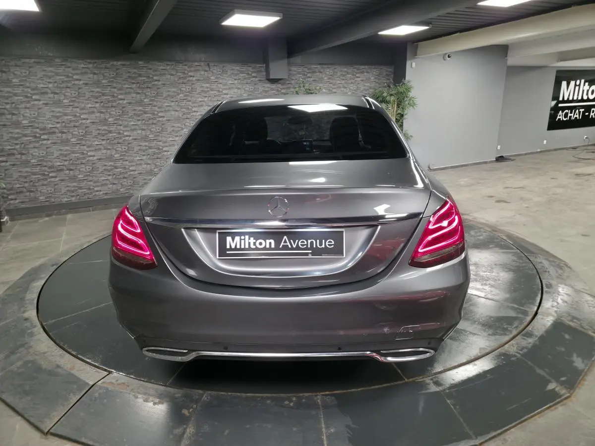 Vue arrière d'une Mercedes Classe C gris métallisé avec feux arrière LED allumés dans un showroom.
