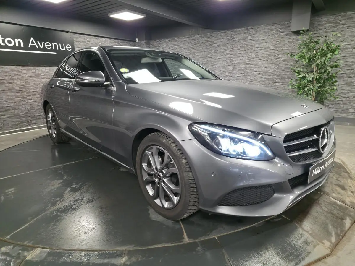 Mercedes Classe C gris métallisé vue 3/4 avant droit avec phares LED allumés en intérieur showroom.