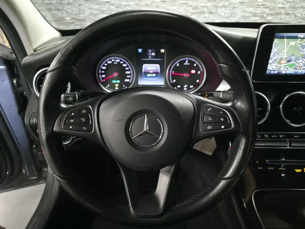 Vue rapprochée du volant noir multifonctions d'une Mercedes Classe C 2018 avec tableau de bord et écran de navigation visibles.