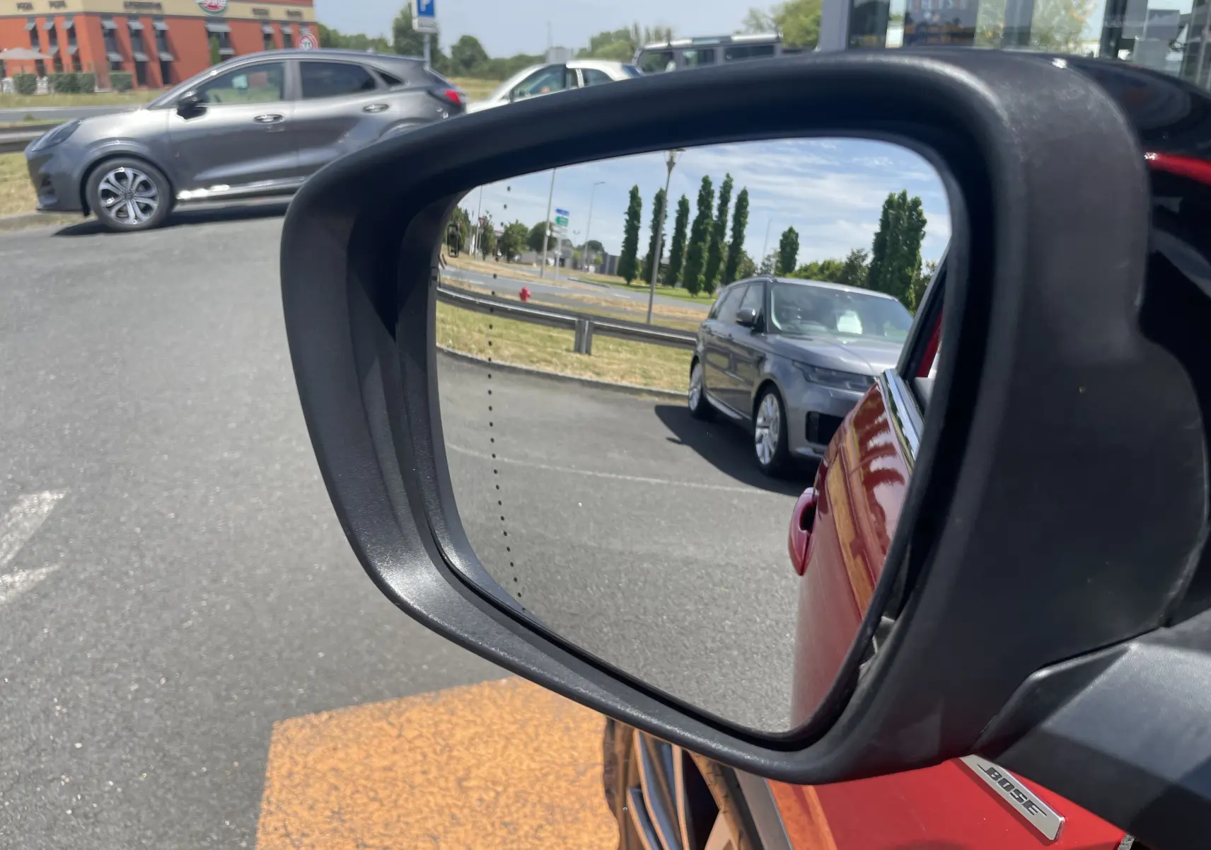 Rétroviseur côté gauche montrant la carrosserie rouge flamme du Renault Kadjar et un véhicule gris en arrière-plan.