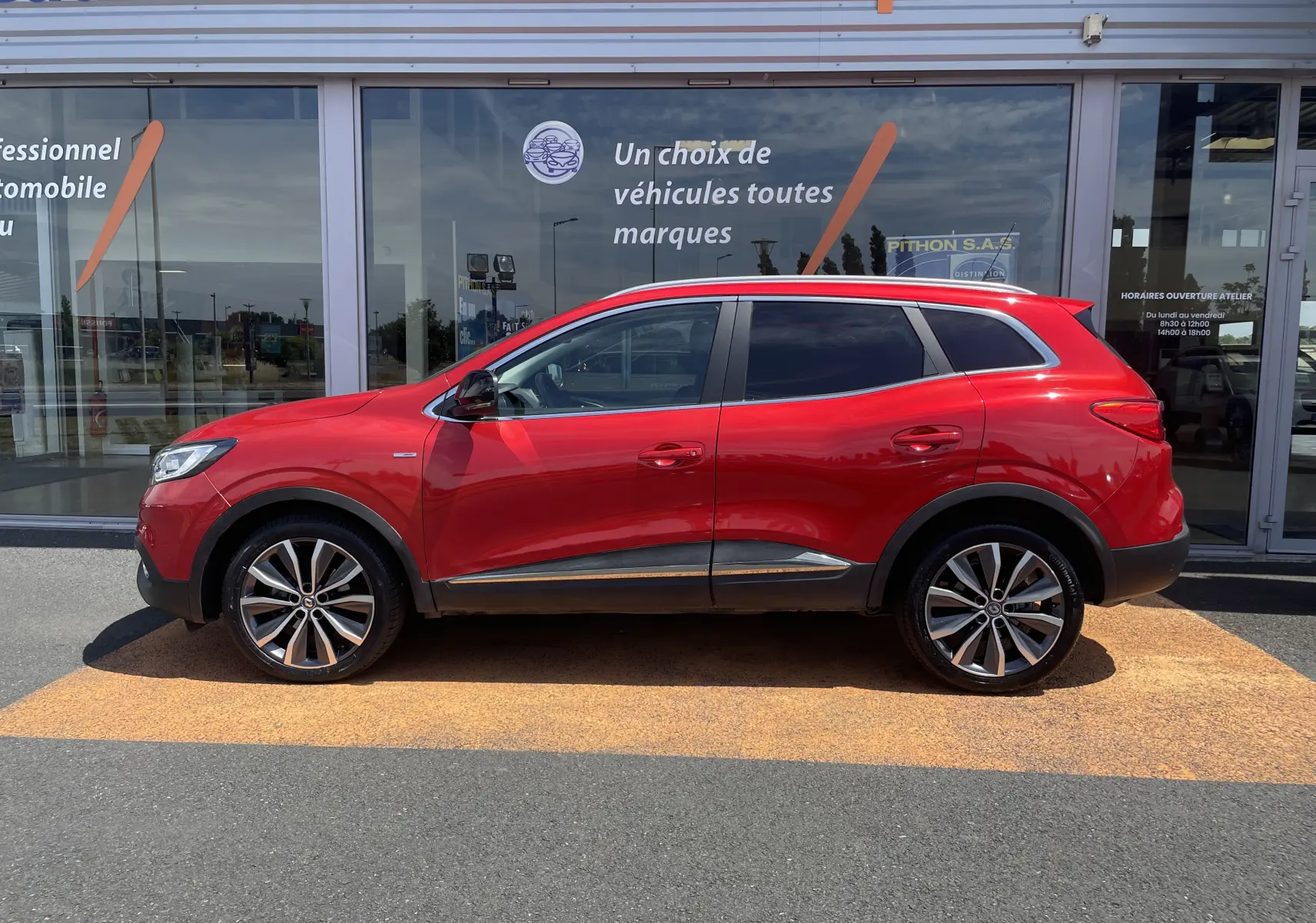 Vue de profil côté gauche d'un Renault Kadjar rouge flamme 2018 avec jantes alliage bicolores et vitres teintées.